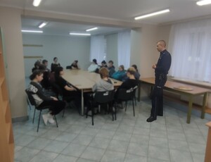 siedzący na krzesłach przy stole słuchacze i stojący przed nimi policjant