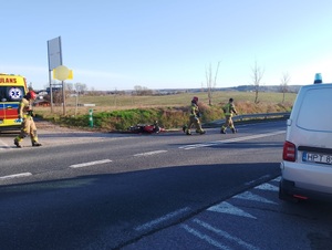 strażacy na miejscu zdarzenia drogowego, w rowie leżący motorower a po prawej stronie stoi na drodze radiowóz