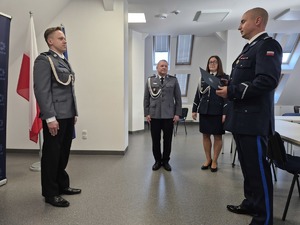 z lewej strony stoi awansowany policjant, przed nim stoi Komendant a w tle kadra kierownicza