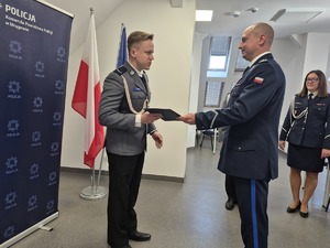 z lewej strony stoi awansowany policjant, Komendant wręcza mu akt mianowania a w tle kadra kierownicza