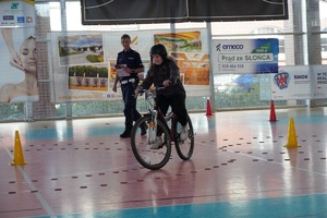 chłopiec jadący rowerem po hali sportowej w tle policjant