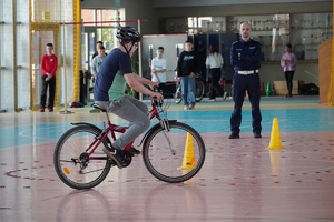chłopiec jadący rowerem po hali sportowej w tle policjant