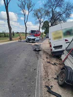 rozbity samochód osobowy stojący na drodze, za nim wóz strażacki, W rowie po prawej stronie widać auto dostawcze