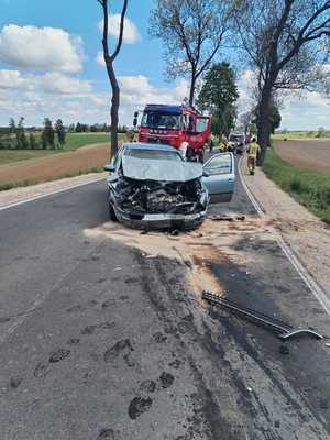 rozbity samochód osobowy stojący na drodze, za nim wóz strażacki