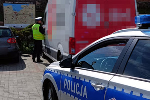 w tle stojący policjant ruchu drogowego przy busie firmy kurierskiej a na pierwszym planie radiowóz