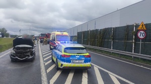 rozbite samochody stojący na drodze i chodzące wokół nich osoby na pierwszym planie stoi radiowóz