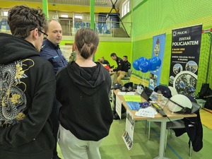 policjant przy stoisku promującym zawód policjanta rozmawia z uczniami