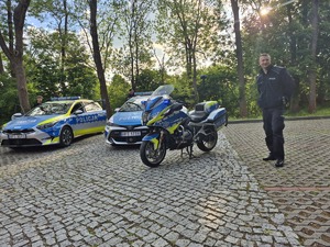 stojący na placu radiowozy i motocykl a przy nich policjant