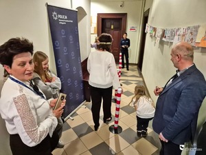 na korytarzu stojące osoby cywilne i policjantka w tle oraz osoba idąca w alkogooglach