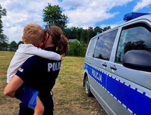 policjantka trzymająca na rękach dziecko, z prawej strony stoi radiowóz