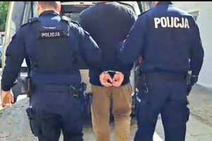 dwóch policjantów prowadzi do radiowozu zatrzymanego mężczyznę, który ma założone kajdanki na ręce