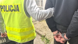 policjant prowadzący osobę zatrzymaną, która ma kajdanki założone na ręce trzymane z tyłu