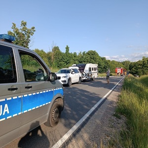 policyjny radiowóz stojący na drodze a w tle widać zdarzenie drogowe