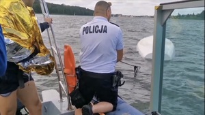 policyjny wodniak na policyjnej łódce za pomocą sznura ściąga łódź, która jest przewrócona w jeziorze do góry dnem