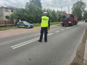stojący na drodze samochód ciężarowy i idący w jego kierunku policjant