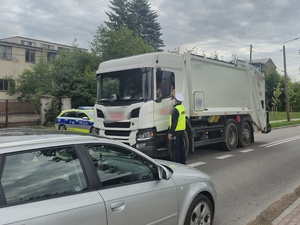 stojący na drodze samochód ciężarowy, stoi obok niego policjant z alkomatem