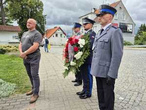 3 policjantów stoi z wieńcem przy nich członek rodziny poległego policjanta