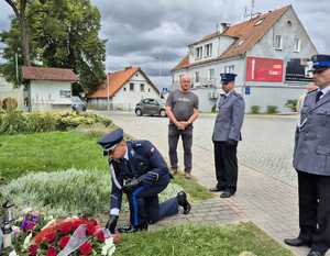 komendant klęka przed obeliskiem i składa wieniec