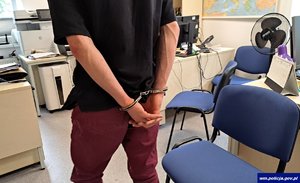 mężczyzna stojący z kajdankami założonymi na ręce trzymane z tyłu