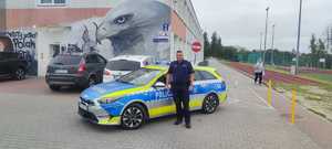 dzielnicowy stojący przy radiowozie na tle szkoły