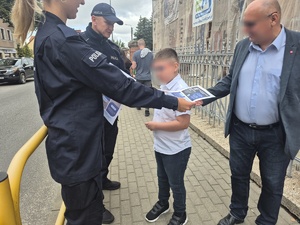 policjant i policjantka rozdają ulotki o bezpieczeństwie i odblaski przy szkole