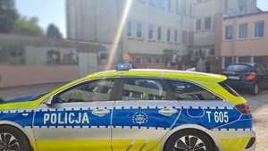 radiowóz stojący przy szkole a w tle uczniowie wychodzący ze szkoły