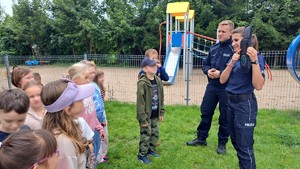 policjantka i policjant stoją przed dziećmi, policjantka pokazuje pomoc dydaktyczną w postaci sygnalizacji świetlnej