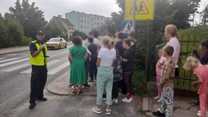 policjant w uczniami przed przejściem dla pieszych