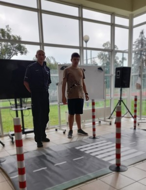 policjant na sali stoi obok ucznia przed nimi rozłożone na podłodze przejście dla pieszych