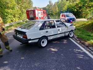 biały samochód marki polonez stojący w poprzek drogi za przed nim wóz strażacki i radiowóz policyjny