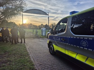 radiowóz stojący przed stadionem a obok niego policjanci