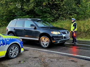policjant stojący na drodze, kontroluje pojazd.