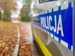 Bok policyjnego radiowozu z widocznym napisem Policja, a w tle jesienna aura