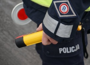 Fotografia przedstawia policjanta ruchu drogowego trzymającego w ręku urządzenie do badania stanu trzeźwości kierujących.