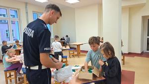 policjant i dzieci stojący przy stole a na stole leżą odblaskowe fragmenty naklejek