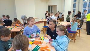 policjant klęczy przy stole przy którym siedzą dzieci a na stole leżą odblaskowe fragmenty naklejek