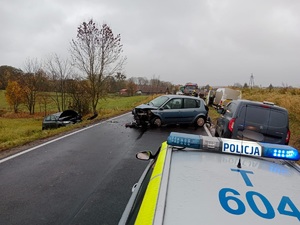 Dach radiowozu a w tle stojące na drodze rozbite 2 samochody i w rowie kolejny rozbity samochód