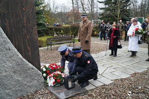 policjant i strażak stawiają przed pomnikiem bukiet oraz znicz, przy nich stoi żołnierz