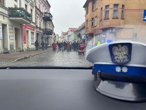 widok z radiowozu, z prawej strony leży czapka ruchu drogowego a przez szybę widać uczestników Marszu Niepodległości