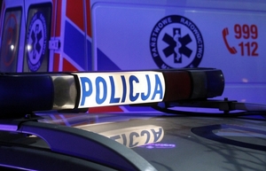 Obrazek przedstawia oznakowany radiowóz policyjny, a w tle widać karetkę pogotowia