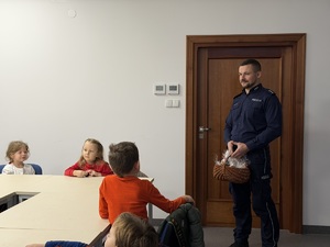 Policjant stoi z koszyczkiem ze słodyczami przed dziećmi