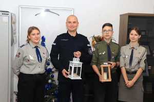 Komendant trzyma lampion z zapaloną świeczką, obok niego stoją harcerze ze swoim lampionem