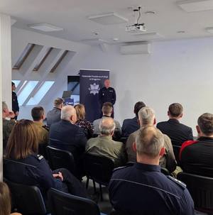 osoby siedzące na sali odpraw a przed nimi stoi Zastępca KWP w Olsztynie