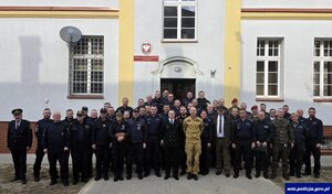 Zdjęcie przedstawia uczestników narady służb odpowiedzialnych za bezpieczeństwo w regionie na tle budynku Oddziałów Prewencji w Olsztynie.
