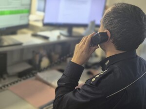 Zdjęcie przedstawia dyżurnego Policji rozmawiającego przez telefon.