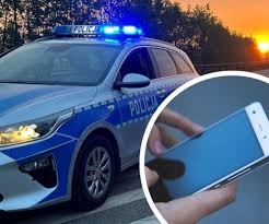 Zdjęcie przedstawia radiowóz policyjny z włączonymi sygnałami oraz małą fotografię przedstawiającą telefon komórkowy.