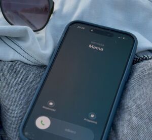 Zdjęcie przedstawia telefon pozostawiony na ubraniach na pomoście nad jeziorem. Na wyświetlaczu telefonu widoczne jest połączenie przychodzące z napisem "Mama".