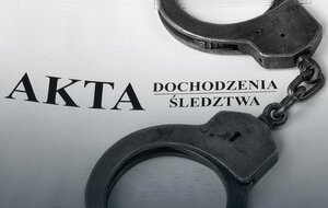 Na zdjęciu znajduje się teczka z napisem AKTA , na której leżą kajdanki.