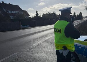 Zdjęcie przedstawia policjanta ruchu drogowego mierzącego prędkość.