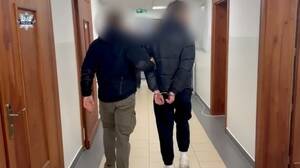 Zdjęcie przedstawia funkcjonariusza policji prowadzącego osobę zatrzymaną.